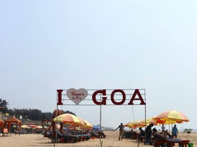 The iconic Aguada Fort overlooking the vast blue Arabian Sea, with golden sands and palm trees lining the coast of North Goa