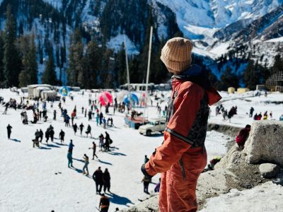 A breathtaking panoramic view of Rohtang Pass, featuring deep snow walls, majestic Himalayan peaks, and tourists enjoying snow activities under a clear blue sky