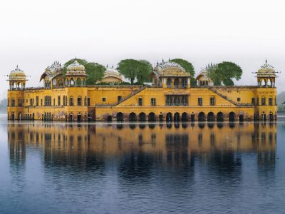 The majestic Amer Fort in Jaipur reflected in Maota Lake at sunset, showing intricate Rajput architecture and massive stone walls under a golden sky